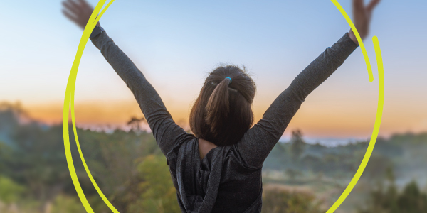 Women holding up her hands on top of a hil overlooking a sunset